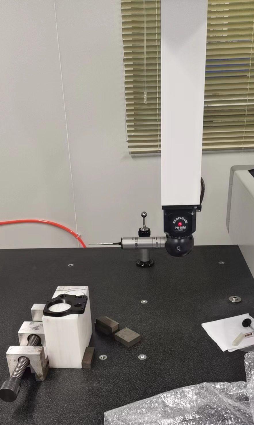 A coordinate measuring machine probe head above a granite surface plate, with a part clamped in a vice and gauge blocks set out beside it.