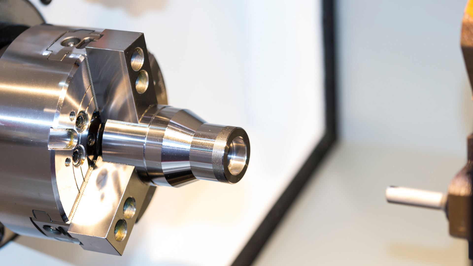A stepped shaft with a threaded end held in a three-jaw chuck, with the tool holder to the right, inside an enclosed lathe.