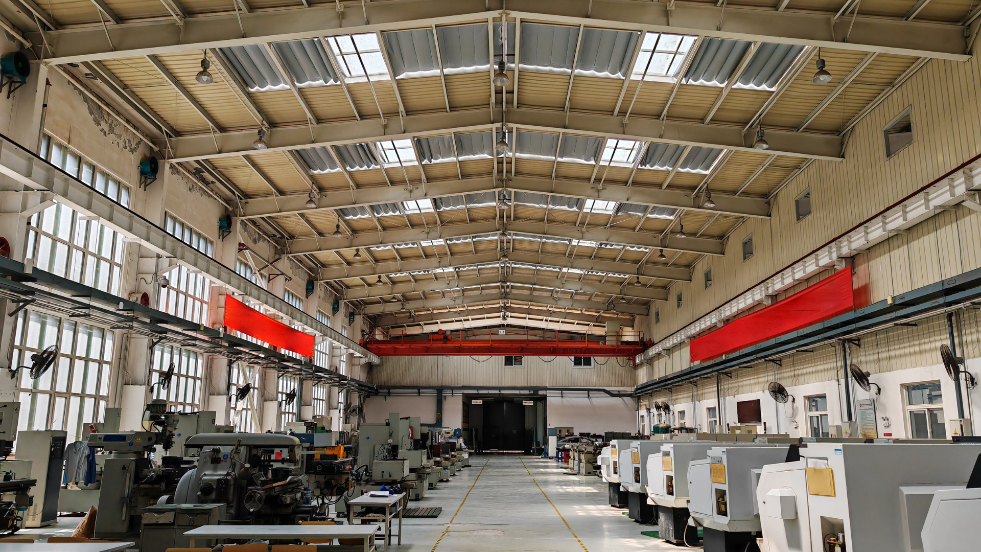 AMPROTO PRECISION workshop floor: a red overhead gantry crane spans the bay between a row of manual machines and a row of enclosed CNC machining centres, with yellow walkway lines on the floor.